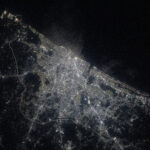 A view of Chennai at night from the International Space Station shows a sprawling city along the water (upper right). City lights make the city shine while also highlighting roadways. The surrounding area is mostly dark.