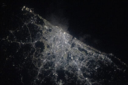 A view of Chennai at night from the International Space Station shows a sprawling city along the water (upper right). City lights make the city shine while also highlighting roadways. The surrounding area is mostly dark.