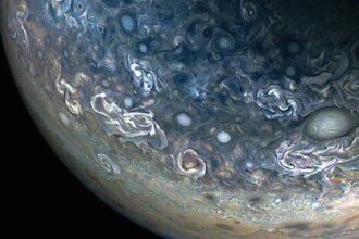 Three quarters of Jupiter can be seen in this photo; the darkness of space covers the bottom of the image. Green and blue swirls cover the planet's surface.