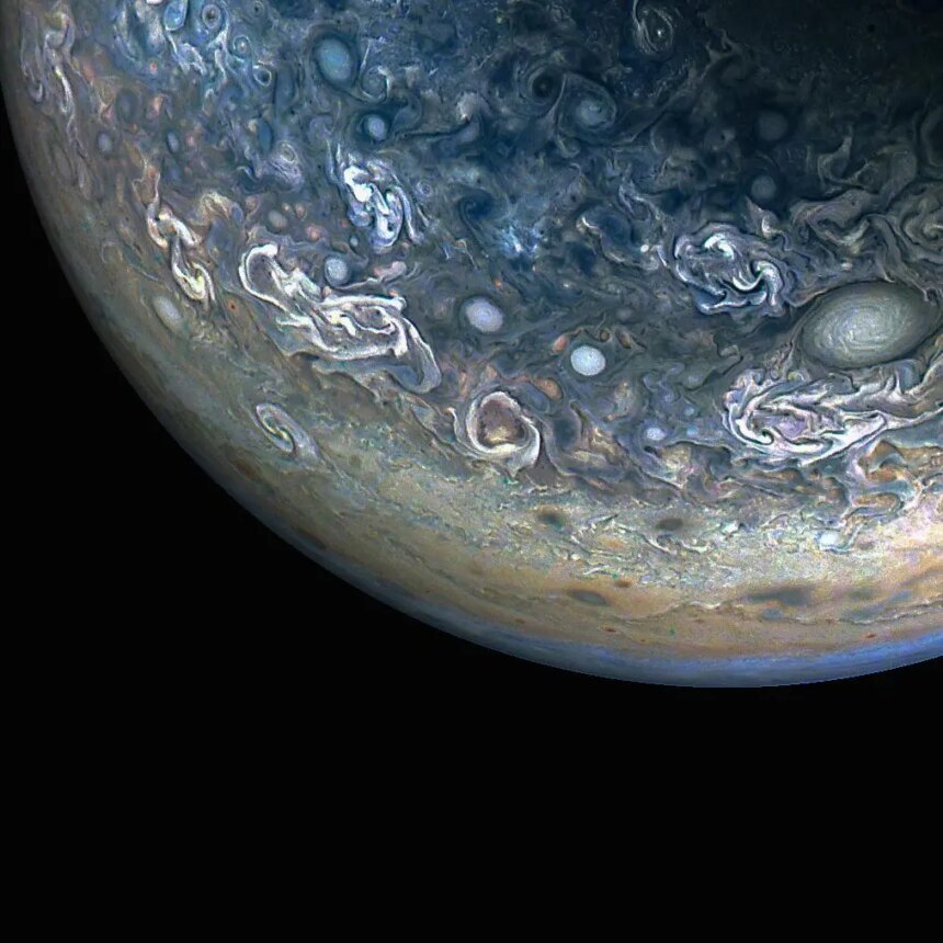 Three quarters of Jupiter can be seen in this photo; the darkness of space covers the bottom of the image. Green and blue swirls cover the planet's surface.