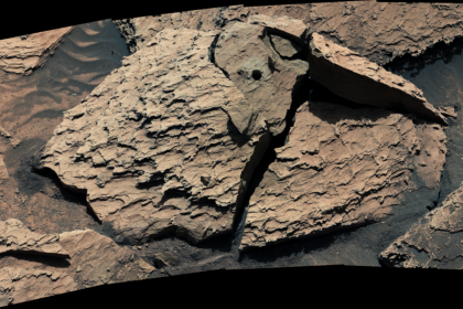 A large, reddish-brown rock as seen by NASA's Curiosity Mars rover. The rock is broken into several pieces. A drill hole is visible in the top middle piece.