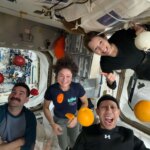 NASA astronauts Jack Hathaway (bottom left), Jessica Meir (middle left), and Chris Williams (bottom right), and ESA (European Space Agency) astronaut Sophie Adenot (top right) pose for a group photo aboard the International Space Station, as fruits and vegetables float around them.