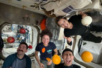 NASA astronauts Jack Hathaway (bottom left), Jessica Meir (middle left), and Chris Williams (bottom right), and ESA (European Space Agency) astronaut Sophie Adenot (top right) pose for a group photo aboard the International Space Station, as fruits and vegetables float around them.