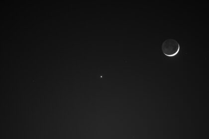 The Moon (right) and Venus (the small dot of light at center) shine above the lit-up Washington Monument at night. Only a small sliver of the Moon is visible.