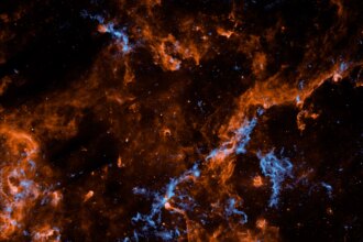 Wispy filaments of vibrant orange and electric blue cosmic dust and gas weave through a dark, star-studded expanse of outer space, creating a chaotic and intricate web of celestial matter.