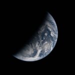 Image of Earth split by the terminator line. The terminator divides Earth’s surface diagonally, shrouding the top left half in darkness. Earth’s illuminated surface is mostly blue and covered in swirling white clouds.