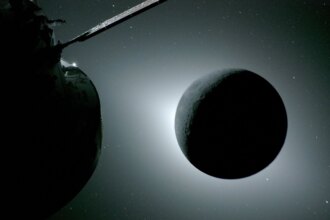 The Moon is backlit by the Sun. Earth is reflecting sunlight at the left edge of the Moon, which is slightly brighter than the rest of the disk; this light reveals a small sliver of the Moon's gray surface. The bright spot visible just below the Moon’s bottom right edge is Saturn. Beyond that, the bright spot at the right edge of the image is Mars. The Orion spacecraft is visible in the foreground on the left.