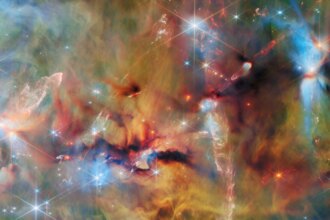 An area inside a star-forming molecular cloud. The background is covered with layers of gas and dust in blue, green and yellowish colors. Thicker clumps of cold dust, dark brown to black, block out light completely. Stars lie among and atop the clouds, from small orange ones to large white or blue ones. Waves and streams of glowing whitish gas are created by jets from protostars colliding with the surrounding material.