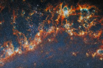 A large, long portion of one of the spiral arms in galaxy M51. Red-orange, clumpy filaments of gas and dust that stretch in a chain from left to right comprise the arm. Shining cyan bubbles light up parts of the gas clouds from within, and gaps expose bright star clusters in these bubbles as glowing white dots. The whole image is dotted with small stars. A faint blue glow around the arm colors the otherwise dark background.